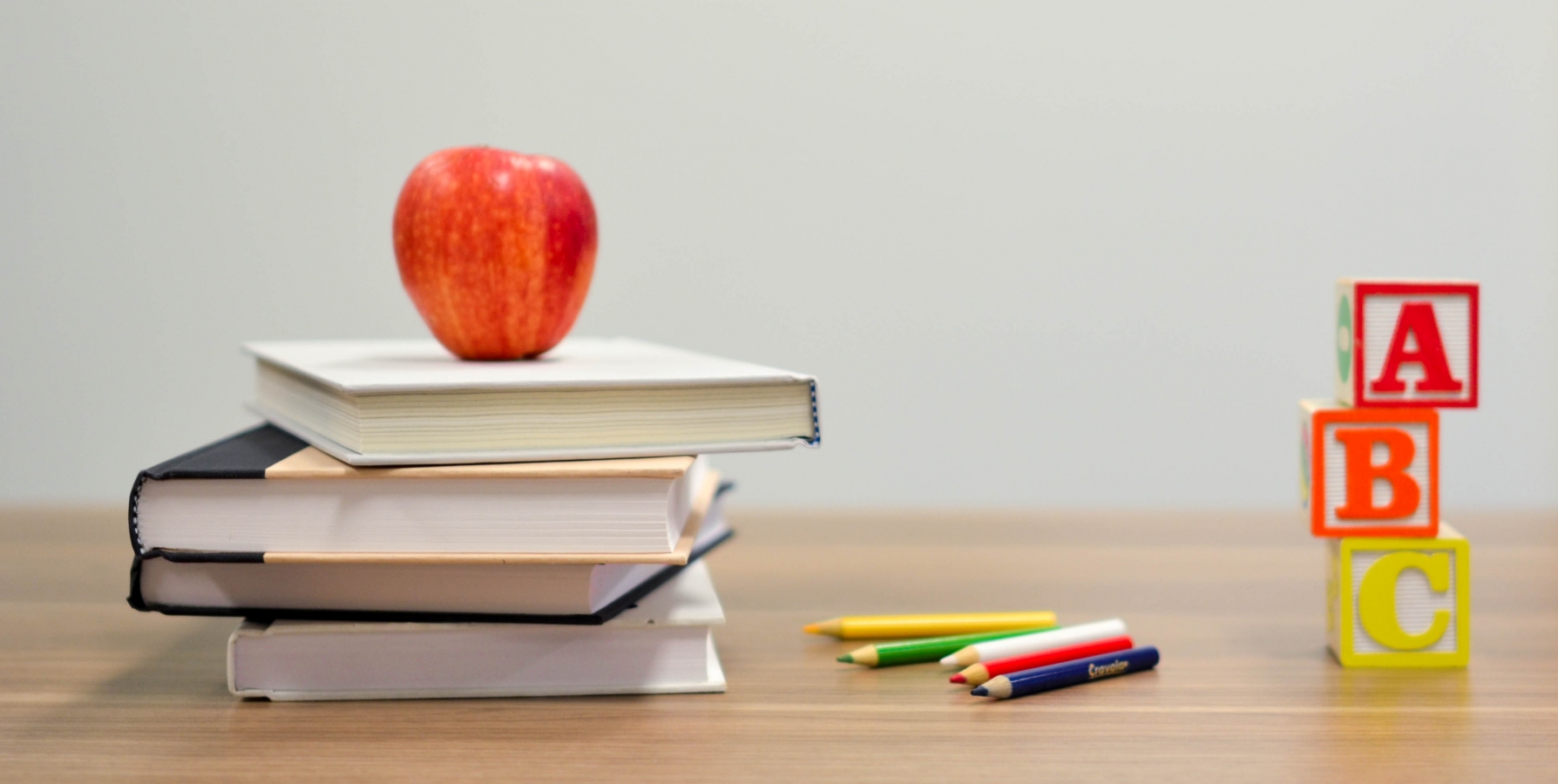 illustrasjon skolestart med en bunke bøker, fargeblyanter og ABC bokstav lekeklosser dandert på en pult, et rødt eple står øverst på bunken av bøker.