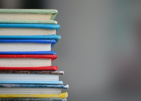 en stabel bøker med forskjellig farge på omslaget mot grå bakgrunn, man ser både omslag og sider da bøkene ligger med ryggen til venstre