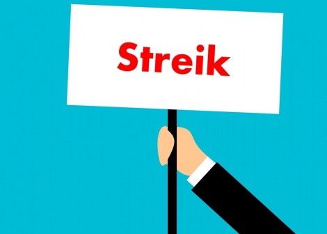 en tegnet hånd holdet opp en hvit plakat hvor det står streik i røde bokstaver, plakaten holdes opp mot en blå bakgrunn